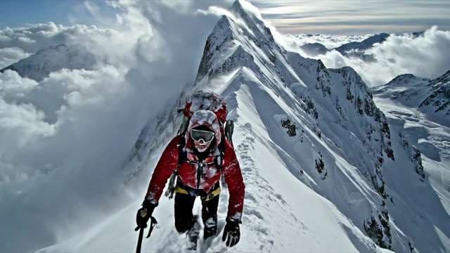 Alpinist Climbing Snowy Mountain Ridge Above the Clouds