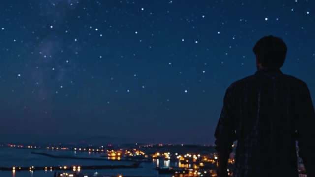 Silhouetted Man Gazing at Starry Sky Above Night City Lights