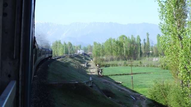 Scenic Train Journey Through Green Valley and Snowy Mountains